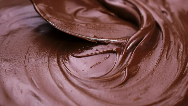 Spoon spreads brown creamy melted milk chocolate paste close up
