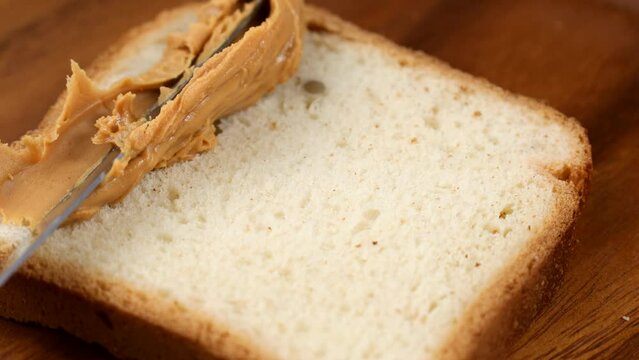 Knife spreads creamy peanut butter on a toast bread close up