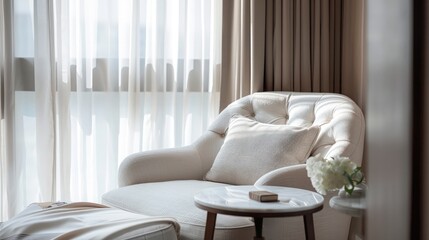 Close-up of a cozy reading corner with a white armchair and small table next to a window with sheer curtains in a hotel room