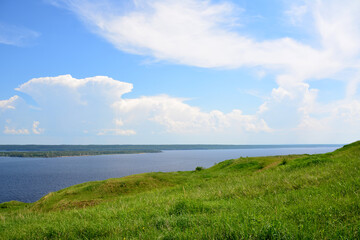 a grassy hill with a lake in the background and a blue sky with clouds  