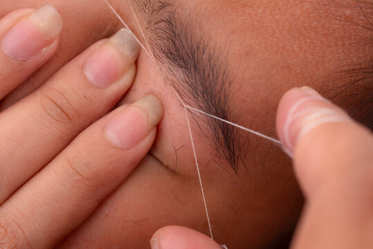 Closeup of an eyebrow threading technique being performed. A precise hair removal procedure using cotton thread for shaping eyebrows.