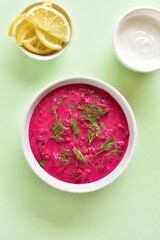 Cold summer beetroot soup in bowl over green background