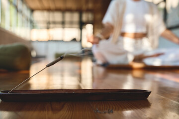 Scented stick on a wooden stand holder. Burning aromatic incense smoky stick with meditating person woman doing yoga on background. Aromatherapy smoke for yoga and meditation healing practices concept