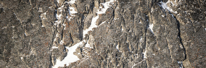 Rock texture. Snow and cracks on the surface of the cliff. Natural stone background.