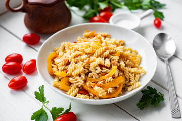 Hearty lunch: pasta with vegetables in a white plate on a white background. Close-up.