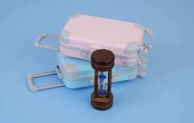 Pink and blue travel suitcases with hourglass on blue background. Vacation time concept. 