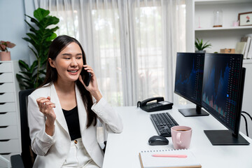 Smiling young beautiful Asian businesswoman calling to broker with raising fist up to make high...