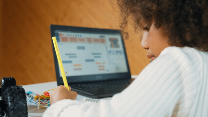 African girl moving touch pad while using laptop programing code and writing prompt code in STEM education. Children learning to designing setting engineering prompt at school. Top view. Erudition.