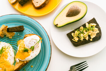 Poached eggs on a toasted slice, bread or toast on a turquoise plate, next to avocado, cheese, tomatoes and cutlery. Delicious and healthy breakfast. View from above.