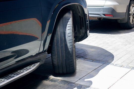A car with a flat tire is parked beside another car in the parking lot