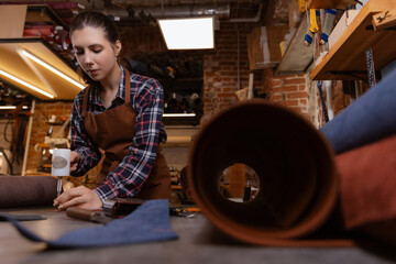 Young woman tailor cutting brown leather patterns in atelier workshop. Concept small business footwear industry, shoemaker