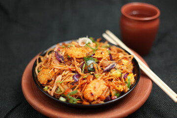Udon noodles spiced with vegetables presented in a traditional way in mud plate. Mud cup with water is placed aside