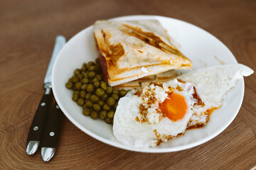 breakfast scrambled eggs hot sandwich with ham and cheese, green peas, legumes on plate