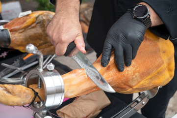 Close-up of a Spanish Chef slicing Iberian ham with a knife and wearing black gloves