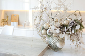 A luxury silver vase with white branches and balls stands on a table in a white kitchen interior
