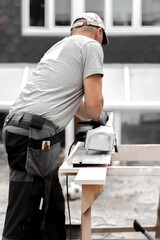 A young man is sawing a board with an electric saw.