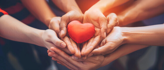 Multiple hands surround and protect a red heart, radiating themes of love, unity, and community spirit in a warm, shared moment.