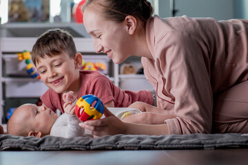Happy mother playing with little children of different ages. Family at home.