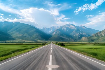 Naklejka premium A wide road leads into the distance, with green fields on both sides and snow-capped mountains in the background. The blue sky is clear, and white clouds float across it