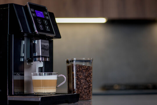Modern coffee machine with glass cup of latte in kitchen