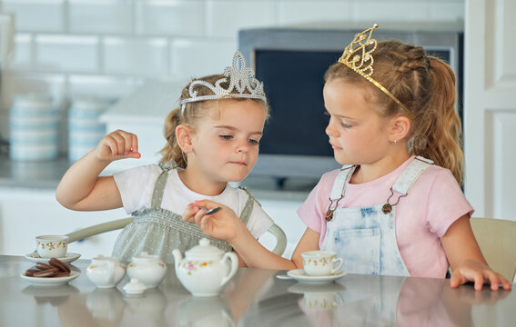 Girl, children and playful in kitchen with tea party for childhood fun, cookies and tiara for pretend. Kids, siblings and toys in home together with love or care, bonding and growth or development. - Powered by Adobe