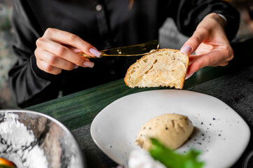 Hands spreading butter on a slice of bread with a butter dish and flour on the table
