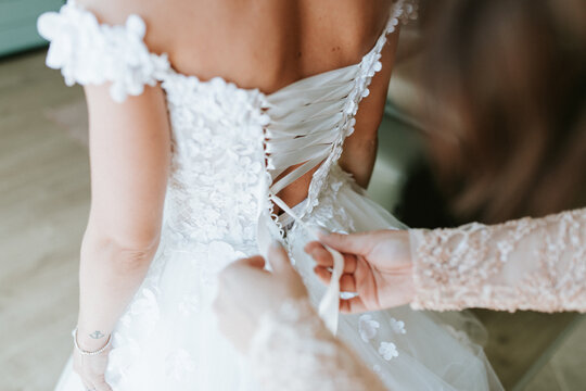 A bride or bridesmaid carefully adjusts the laces or buttons of a wedding dress, highlighting the detailed preparations and anticipation before the ceremony.