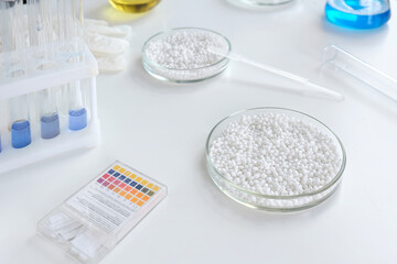 Close-up of a laboratory Petri dish with white granules against the background of chemical tools and utensils.