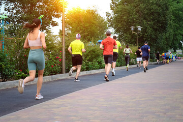 City marathon runners run along a pedestrian path in a city park.