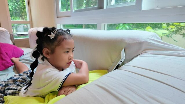 Small girl in school uniform lying on counch looking at tablet.