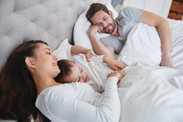 Fototapeta premium Mother, son and father in bedroom, hug and bonding with love, man and woman with care for boy in home. Mom, dad and kid together on bed, happiness and relax in weekend, parents and child in house