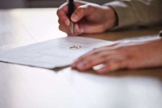 Ring, hands and divorce papers for signature on legal paperwork on table to end marriage. Wedding band, pen and man writing information on document for separation with jewelry for breakup decree.