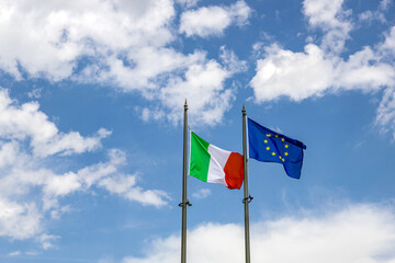 Flags of Italy and European Union waving in the wind. Blue sky with clouds in the background