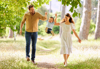 Obraz premium Smile, family and swinging child outdoor park together for bonding, love and support on summer vacation. Woman, man and kid play with care, trust and walking holding hands for freedom on holiday