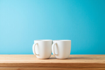 White coffee cups on wooden table over blue background. Mockup for design and branding