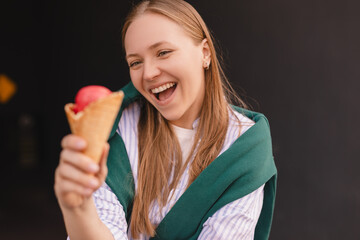 Joyful adorable teenage girl with blonde hair hold tasty ice cream smiles broadly has fun enjoys in stylish clothes isolated on black wall. Happy wow girl with gelato, look at ice cream.