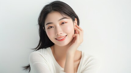 Fototapeta premium Beautiful Asian woman with flawless skin smiling and touching her face, isolated on a white background. Studio shot for beauty and spa services, showcasing perfect skin and happiness. 