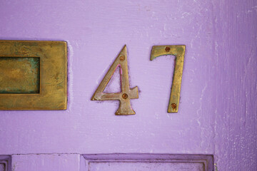 Antique Ddoor number 47 in rusty gold metal on a bright lilac painted door
