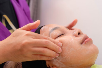 A woman enjoys a relaxing facial massage with cream at a beauty spa, preparing for facial or ultrasound scrubbing.