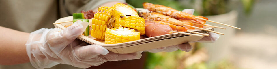 Header with woman holding tray with grilled vegetables, shrimps and sausages