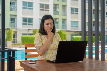 Woman using laptop computer and wearing yellow floral dress outdoors with swimming pool background