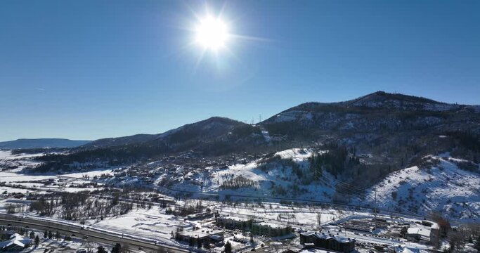 amazing drone shot with sun shining down on mountain town with many buildings and cabins covered in snow in winter
