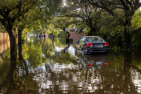 After the 2024 Hallandale Beach flood, a car is submerged in floodwaters outside a suburban home. Reflections in the water emphasize the severe impact on residential areas and the need for recovery.
