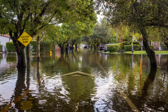 After the 2024 Hallandale Beach flood, a car is submerged in floodwaters outside a suburban home. Reflections in the water emphasize the severe impact on residential areas and the need for recovery.