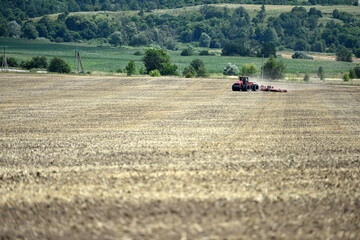 Fototapeta premium Kyiv, Ukraine, 19.07.2023. Red tractor with a plow on an agricultural field. work in the field. farmland, tractor in the field. mechanism, Tractor plowing land. Harvester sowing wheat. Editorial