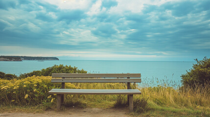 Obraz premium Empty bench overlooking a tranquil ocean with cloudy sky