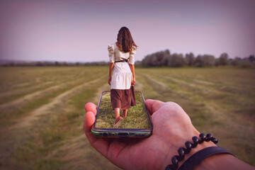 A woman is walking across a field that is inside a phone.
A woman walks through a field of tall grass as she is captured in a phone screen held by an outstretched hand.