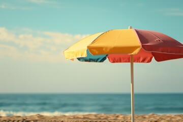 A colorful beach umbrella provides shade on a sunny day, standing tall on the sandy beach. The umbrella's vibrant hues pop against the neutral tones of the shore.