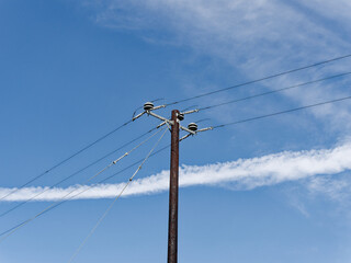 An aged power pole with lines against a blue sky with clouds, symbolizing enduring connectivity.