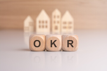 letters OKR on wooden blocks and house models on background, concept for Objectives and Key Results